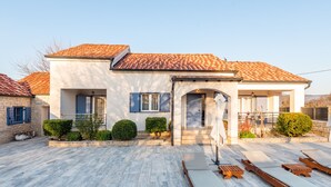 A modern house with a tiled roof, a covered patio with lounge chairs, and a well-maintained garden. - Villa Niko with heated pool by Interhome (Pridraga)