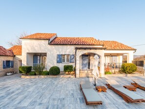 A modern house with a tiled roof, a covered patio with lounge chairs, and a well-maintained garden. - Villa Niko with heated pool by Interhome (Pridraga)