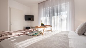 A bedroom with a bed, bedside table, books, a TV, and a window with curtains. - Villa Niko with heated pool by Interhome (Pridraga)
