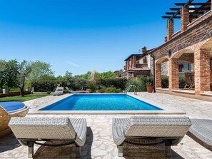 A rectangular swimming pool with a stone deck, surrounded by lounge chairs and a brick building with an arched entrance. - Villa Toscana Sole with pool by Interhome (Bokordici)