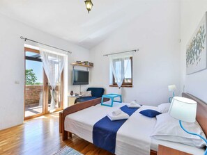 Ein Schlafzimmer mit Bett, Schreibtisch, Sessel, Fernseher und einem Balkon mit Vorhängen.