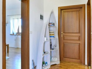 A hallway with a wooden door, a white shelf with books, and a window with sheer curtains. - Vacation home  by Interhome (Bokordici)
