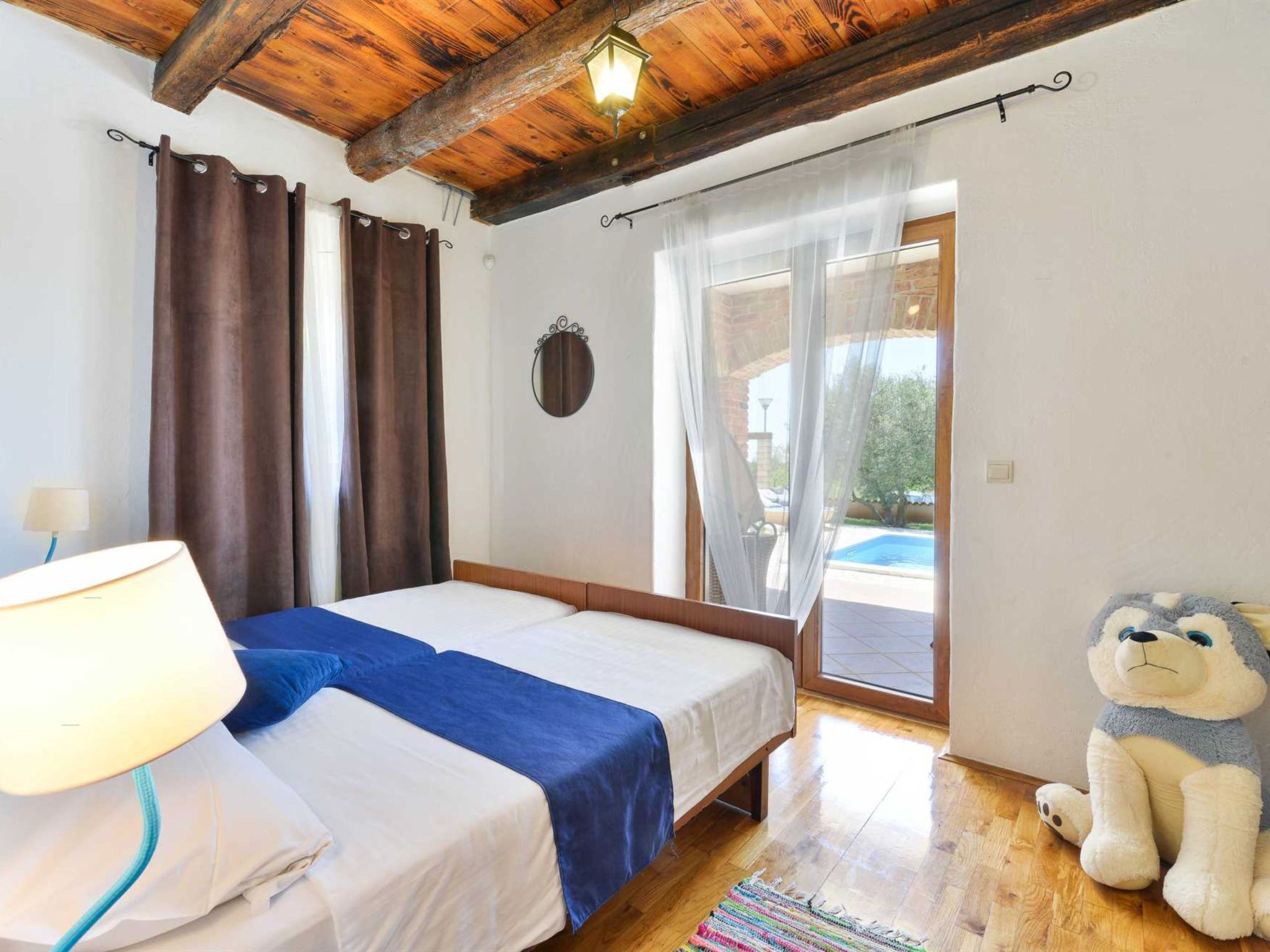 A bedroom with a bed, curtains, a lamp, a stuffed toy, and a view of an outdoor area.