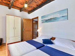 A bedroom with two beds, a wardrobe, and a painting of a seascape. - Vacation home  by Interhome (Bokordici)