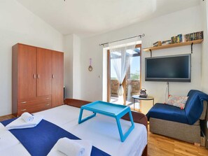 Et soveværelse med seng, fjernsyn, garderobeskab og balkon.