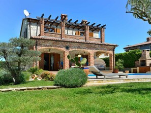 Ein zweistöckiges Haus mit Backsteinfassade, einer Pergola und einem Swimmingpool.