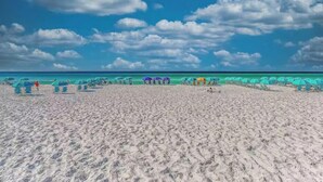 A beach with rows of umbrellas and lounge chairs, a clear sky, and a calm sea. - Beautifully Decorated 2BR 2BA BEACHFRONT Condo! (Miramar Beach)