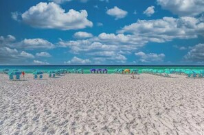 Ein Strand mit Reihen von Sonnenschirmen und Liegestühlen, einem klaren Himmel und einem ruhigen Meer.