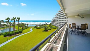 A balcony with a view of the ocean, a pool, and a well-maintained lawn. - Beautifully Decorated 2BR 2BA BEACHFRONT Condo! (Miramar Beach)
