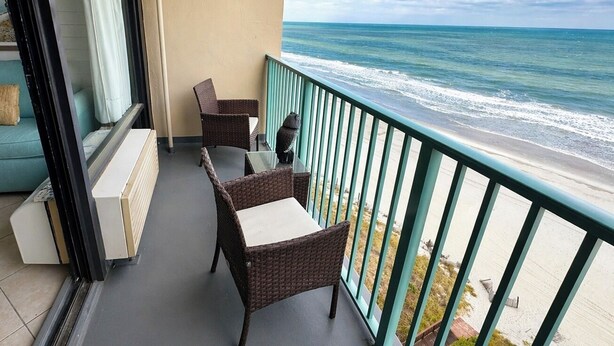 Ein Balkon mit Korbmöbeln, Blick auf den Ozean und einen Strand.