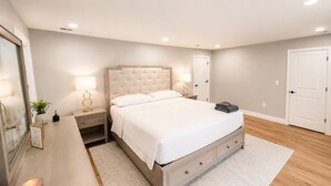 A bedroom with a bed, bedside tables, a nightstand, a mirror, a door, and a wall-mounted light fixture. - Welcome to Seven Oaks:Your Home Away From Home (City of Orange)