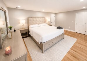 A bedroom with a bed, bedside tables, a nightstand, a mirror, a door, and a wall-mounted light fixture. - Spacious 5-bedroom house in charming City of Orange with AC (City of Orange)