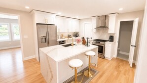 A modern kitchen with white cabinetry, stainless steel appliances, and a central island with stools. - Welcome to Seven Oaks:Your Home Away From Home (City of Orange)
