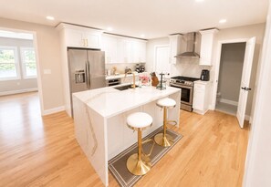 A modern kitchen with white cabinetry, stainless steel appliances, and a central island with stools. - Spacious 5-bedroom house in charming City of Orange with AC (City of Orange)