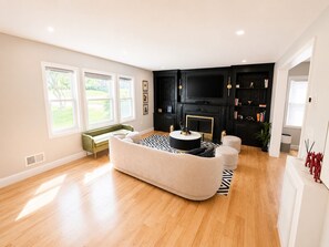 A living room with a sofa, a coffee table, a fireplace, a TV, and a bookshelf. - Spacious 5-bedroom house in charming City of Orange with AC (City of Orange)