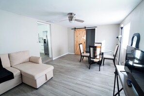 Ein modernes Wohnzimmer mit einer Couch, einem Esstisch mit Stühlen, einem Deckenventilator und einem Fernseher.