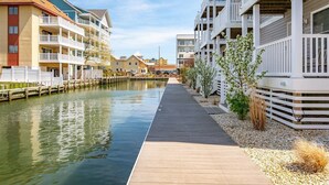 Ein Ufergrundstück mit einer Holzpromenade, mehrstöckigen Gebäuden mit Balkonen und einer ruhigen Wasserfläche.