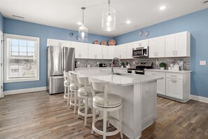 Een moderne keuken met witte kasten, roestvrijstalen apparatuur, een centraal eiland met barkrukken en een blauwe accentmuur.