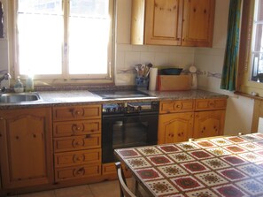 A kitchen with wooden cabinets, a stainless steel sink, a stove, and a table with a patterned tablecloth.