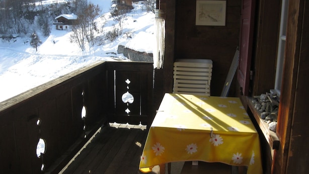 A wooden balcony with a table covered in a yellow tablecloth, overlooking a snowy landscape with houses. - Casa Alpina und Fop Maiensäss, Waltensburg, (Waltensburg/Vuorz), 58011A by Interhome (Surselva)