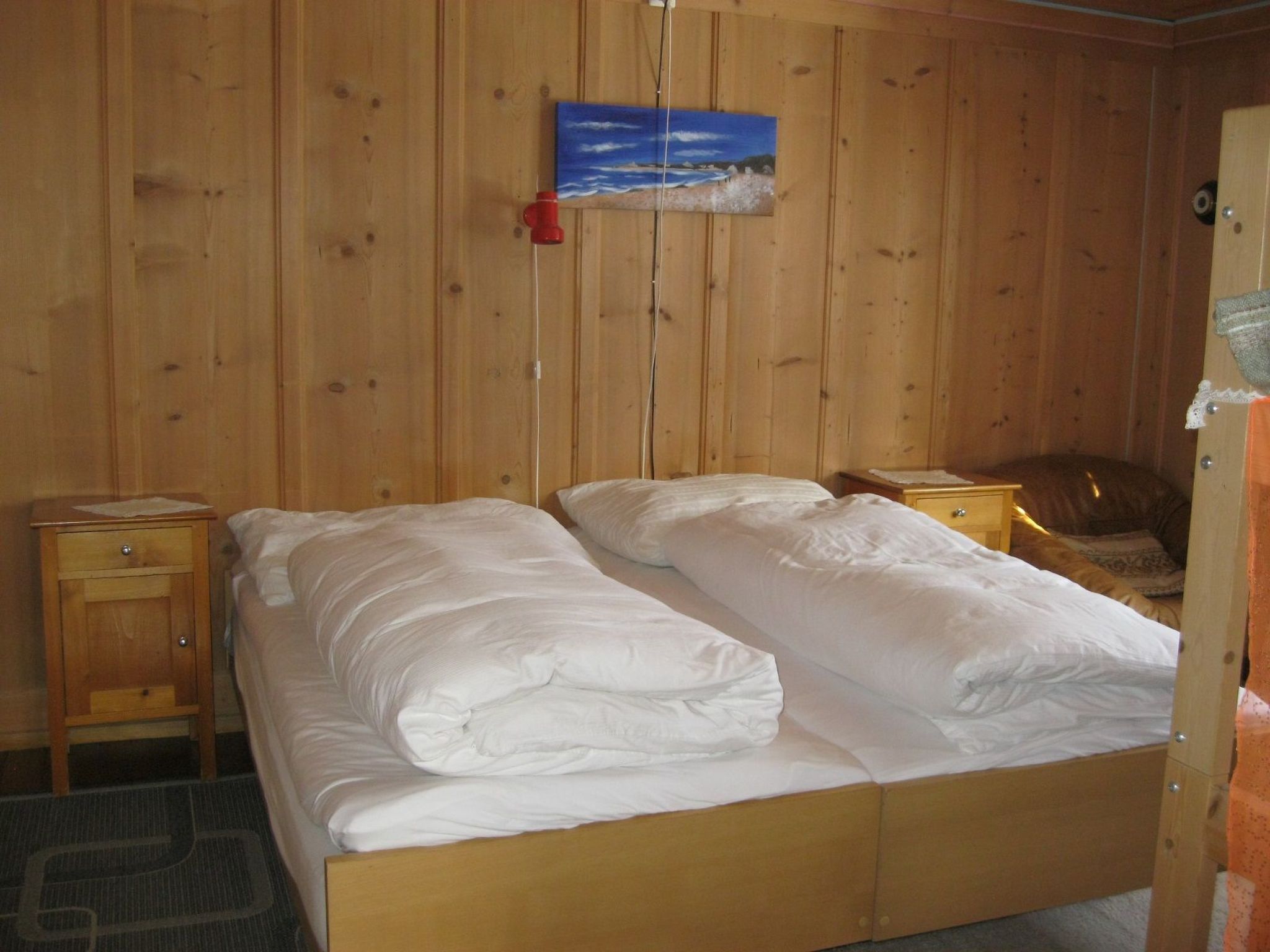 A wooden-paneled room with a bed, two bedside tables, a nightstand, and a painting on the wall.