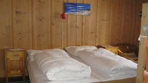 A wooden-paneled room with a bed, two bedside tables, a nightstand, and a painting on the wall. - Casa Alpina und Fop Maiensäss, Waltensburg, (Waltensburg/Vuorz), 58011A by Interhome (Surselva)