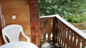 A wooden deck with a white plastic chair and a table, a wooden railing, and a green tree in the background. - Casa Canal 27 Cavegn, Brigels, (Breil/Brigels), 65000B by Interhome (Breil/Brigels)