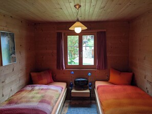 Ein Hotelzimmer mit zwei Betten, einem fenster mit Vorhängen, einer Deckenleuchte und einem kleinen Tisch mit einem Radio.