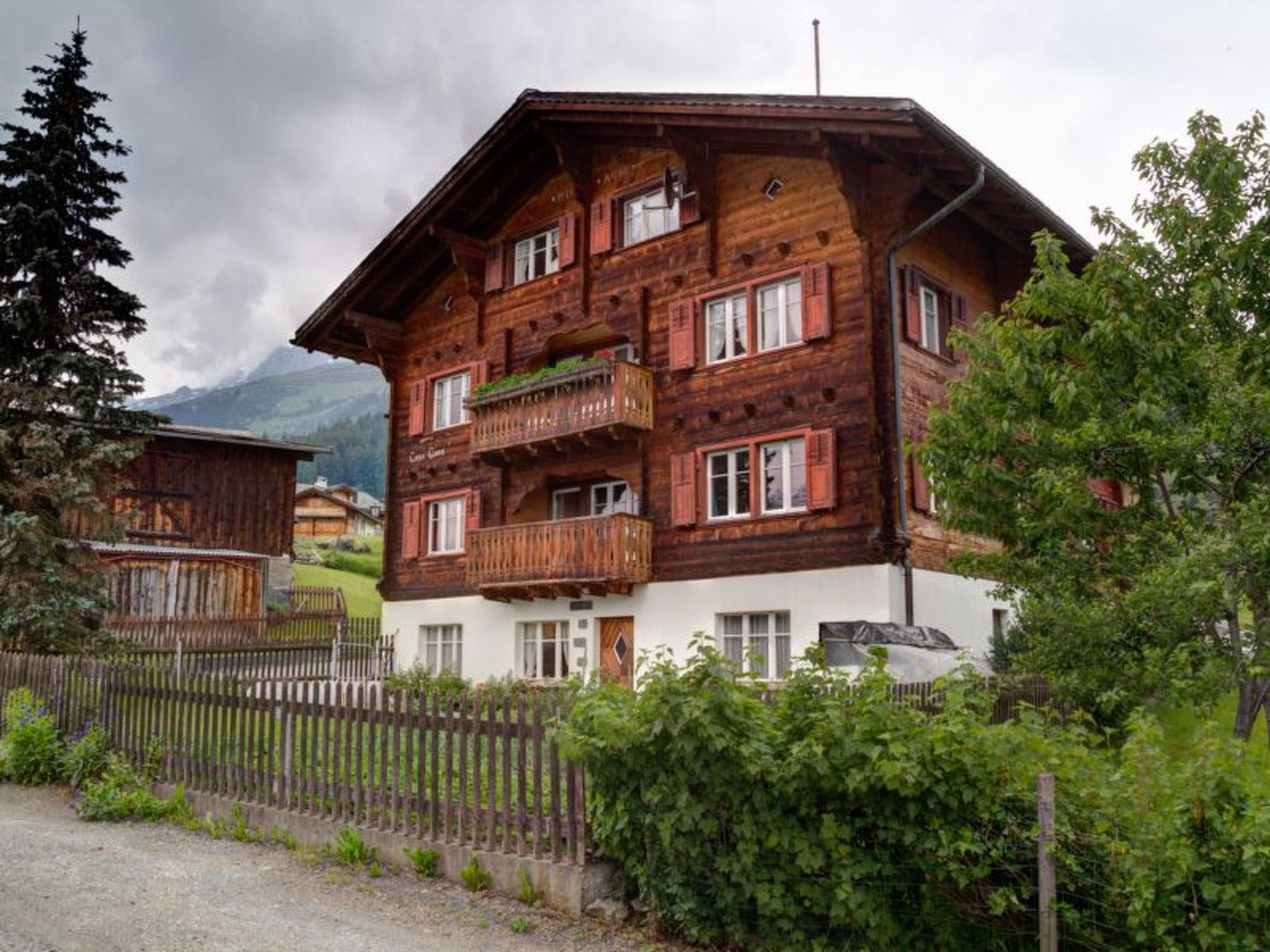 Eine mehrstöckige Holzhütte mit Balkonen, umgeben von Grün und einem Bergpanorama.