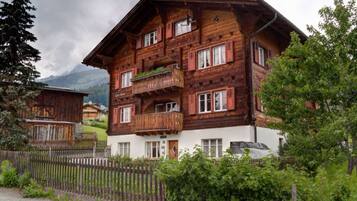 Eine mehrstöckige Holzhütte mit Balkonen, umgeben von Grün und einem Bergpanorama.