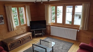 A room with a wooden interior, a television on a stand, a sofa, a glass coffee table, and windows with curtains. - Casa Canal 27 Cavegn, Brigels, (Breil/Brigels), 65000B by Interhome (Breil/Brigels)
