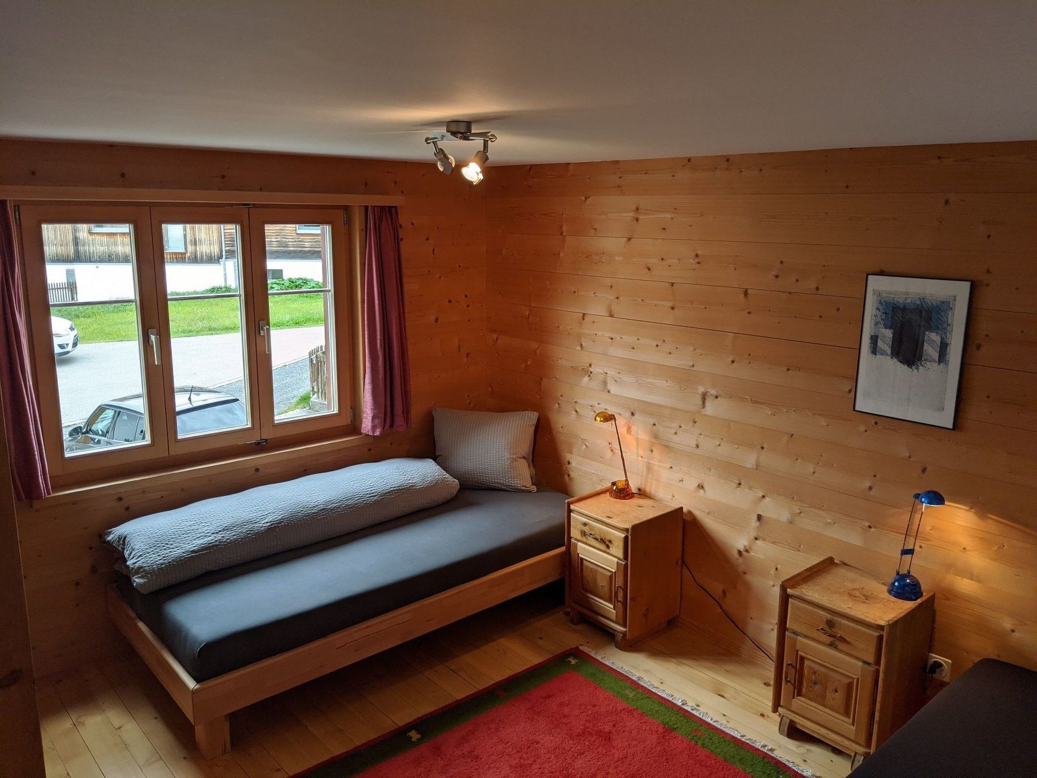 Ein schlichter Raum mit einem Einzelbett, einem Nachttisch, einem Schreibtisch und einem Fenster mit Vorhängen.