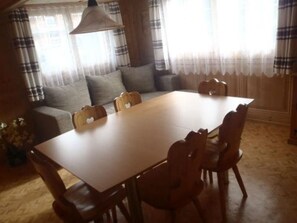Ein Essbereich mit einem Holztisch und Stühlen, einer Couch und einem Fenster mit Vorhängen.