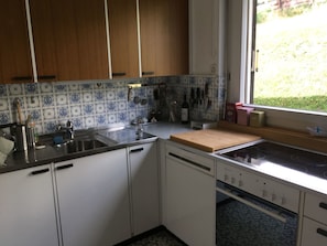 Eine Küche mit weißen Schränken, einer gefliesten Spritzschutzwand, einem Spülbecken, einem Herd und einem Fenster mit Blick auf Grünfläche.
