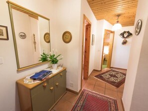 A hallway with a wooden ceiling, a mirror, a dresser with a plant, and a rug. - Casa Panorama Lutz, Brigels, (Breil/Brigels), 65061B by Interhome (Breil/Brigels)