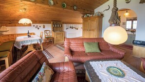 Een gezellige kamer met een houten plafond, een eettafel, een bank en een keukenhoek.