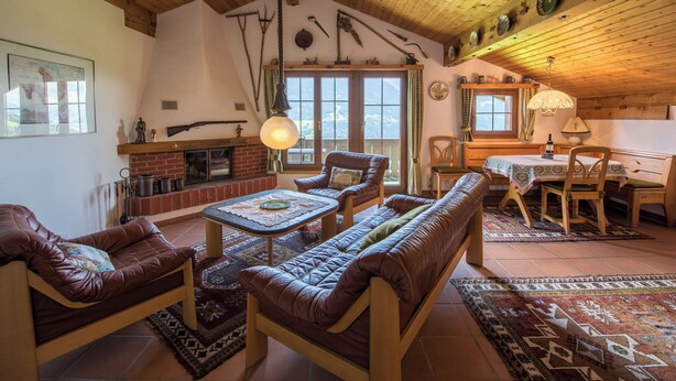Een rustiek interieur met een open haard, lederen zitplaatsen, houten balken en een eethoek.