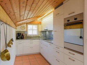 A kitchen with white cabinets, a clock, a window with curtains, and a stove. - Casa Panorama Lutz, Brigels, (Breil/Brigels), 65061B by Interhome (Breil/Brigels)