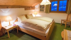 Een houten bed in een kamer met een groen tapijt, een raam met uitzicht op een berg en een lamp op een nachtkastje.