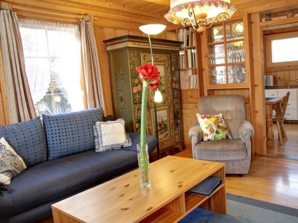 A cozy living room with a sofa, armchair, wooden coffee table, and a vase with a flower.