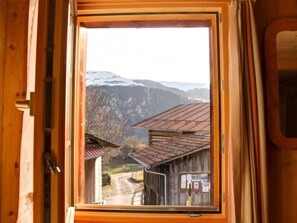 A wooden-framed window with a view of a rural landscape, including buildings and mountains.