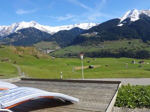 A wooden deck with a view of a green valley and snow-capped mountains. - Ferienhaus Bual da Rumein Wettstein, Rumein, (Degen), 45003B by Interhome (Vattiz)