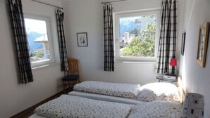 Et værelse med to senge, en stol, et bord med lampe og et vindue med gardiner.