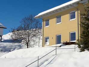 Un bâtiment jaune avec de nombreuses fenêtres, un toit recouvert de neige et un escalier menant à l’entrée.