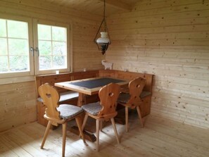 Interior em madeira com mesa de jantar e cadeiras, janela e luminária pendente.