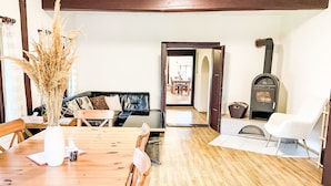 Une table à manger en bois, des chaises, un canapé, une cheminée et une porte donnant sur une autre pièce.