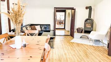 Une table à manger en bois, des chaises, un canapé, une cheminée et une porte donnant sur une autre pièce.