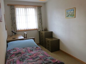 Un dormitorio con cama, escritorio, cómoda y ventana con cortinas.