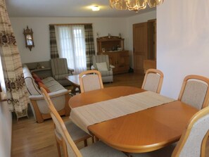 Ein Wohnzimmer mit Esstisch, Stühlen, Sofas, einem Holzkabinett und einer Pendelleuchte.