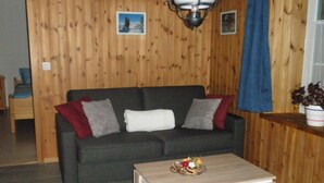 Puupaneloitu huone, jossa on tummanvärinen sohva, pieni pöytä ja sininen verho.